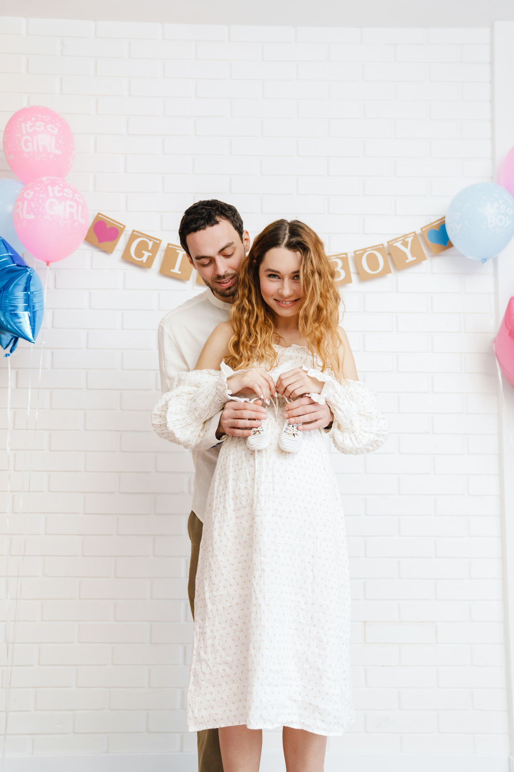 Young Happy Couple Posing with Baby Shoes during Gender Reveal Party